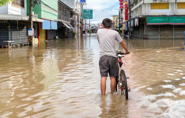 Man walking through a flooded street with his bicycle