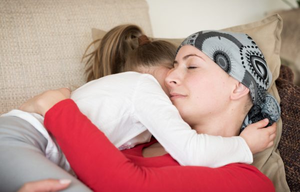 Young adult female cancer patient spending time with her daughter at home, relaxing on the couch. Cancer and family support concept.