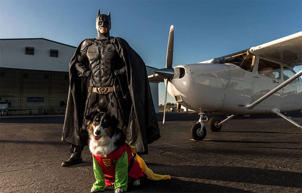 Man and dog dressed as Batman and Robin with a plane in the background