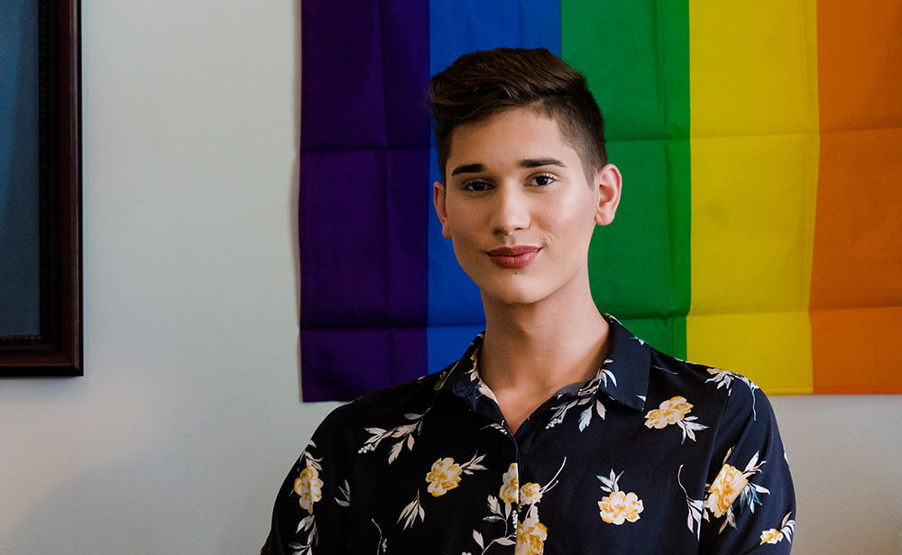 Young man smiling with rainbow flag behind him