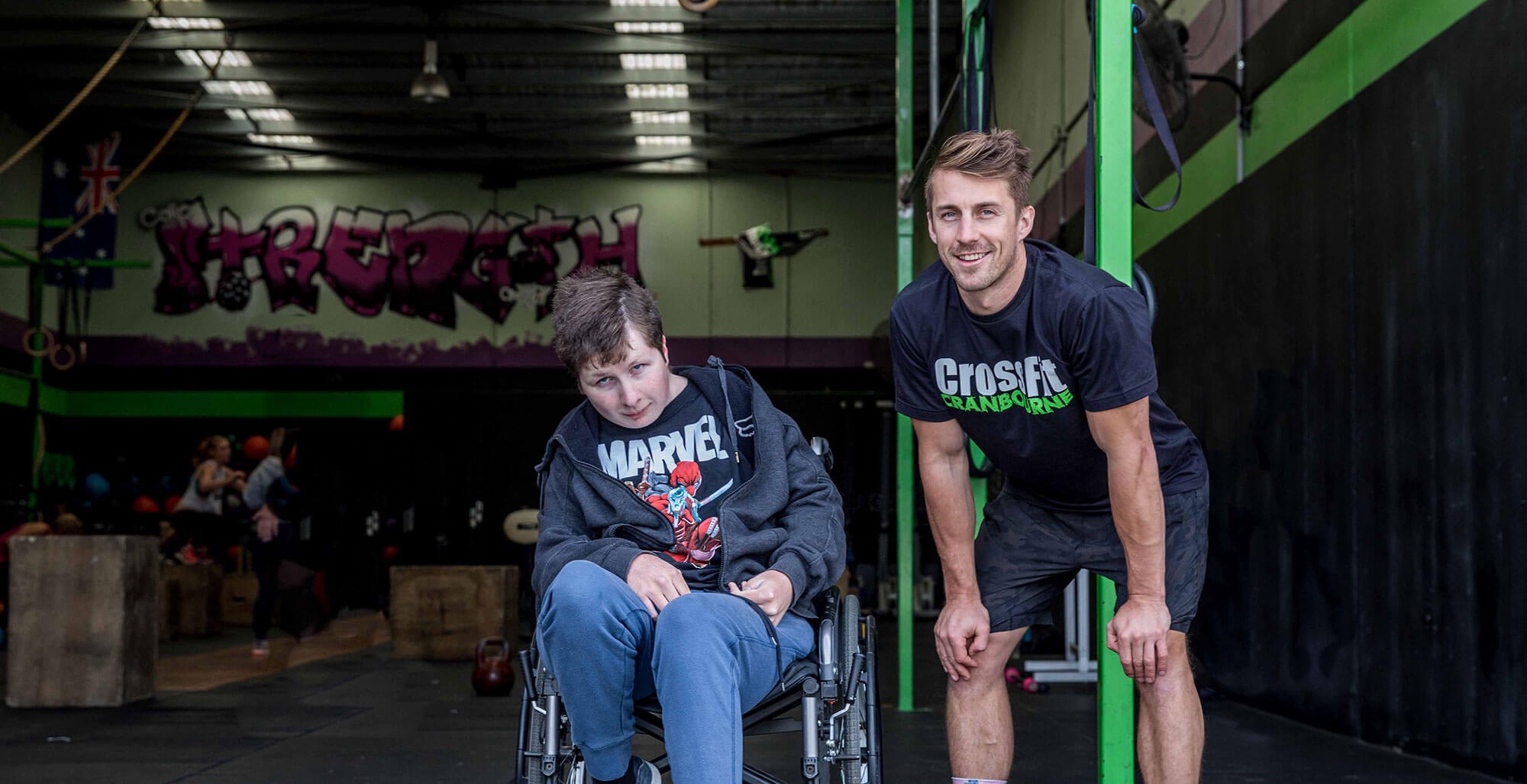 Young boy in a wheelchair with man standing in front of a gym