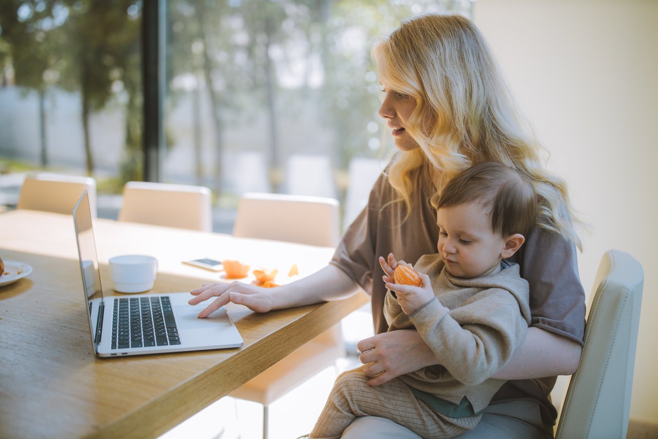 woman-carrying-her-baby-and-working-on-a-laptop-4079281