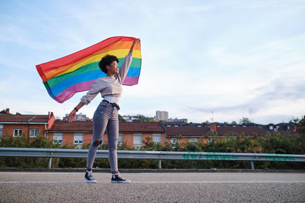 woman smiling and holding a rainbow striped lgbtq+ flag