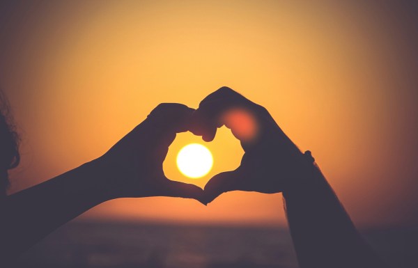 hands making a heart around a setting sun