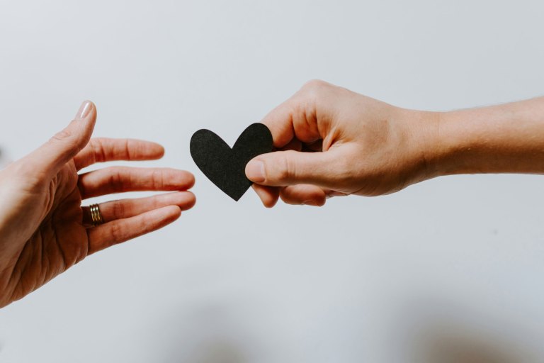 A hand holding out a paper heart to another hand