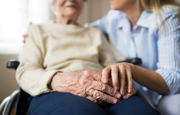 An old person sitting on a wheelchair, holding hands with a family member