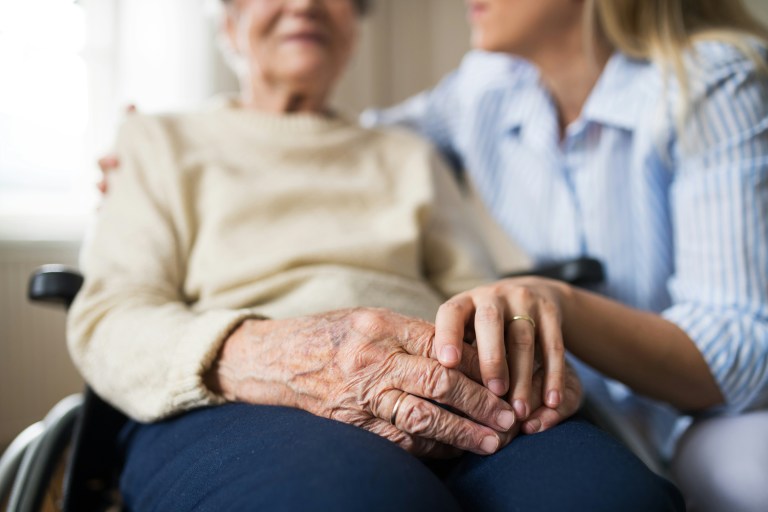 An old person sitting on a wheelchair, holding hands with a family member