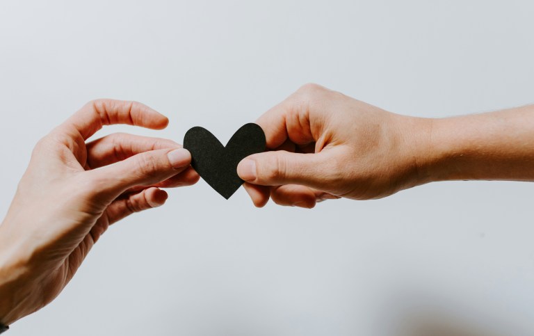 Two hands holding a paper black heart. Photo by Kelly Sikkerna