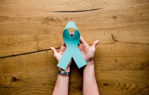 Hands holding a teal ribbon, symbol of ovarian cancer.