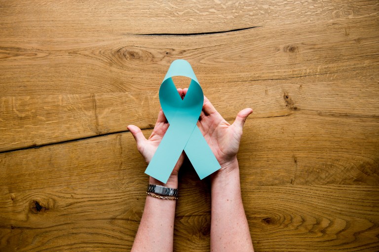 Hands holding a teal ribbon, symbol of ovarian cancer.