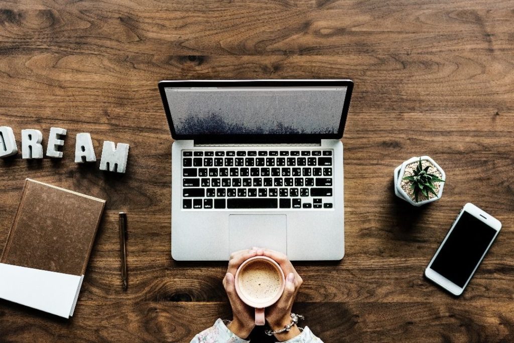 Ordinateur portable sur un bureau avec deux mains tenant un café