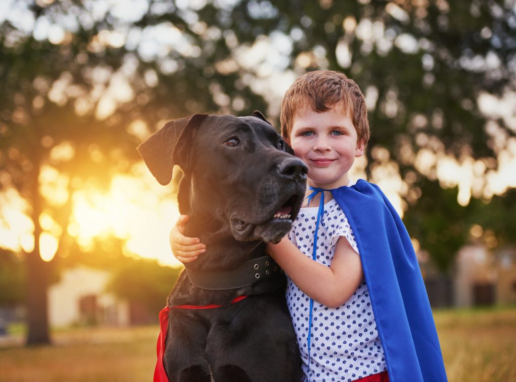 Shot of a little boy and his dog wearing capes while playing outside
