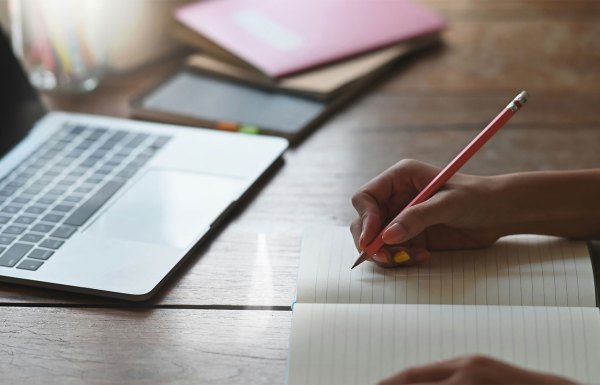 A person writing down a drafted email with a pencil and paper