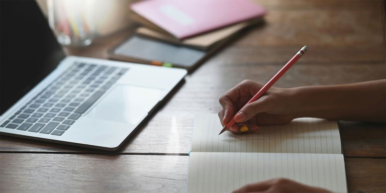 A person writing down a drafted email with a pencil and paper