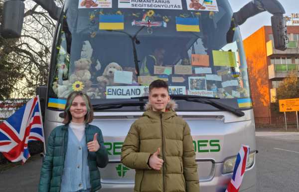 Kids give a thumbs up in front of bus