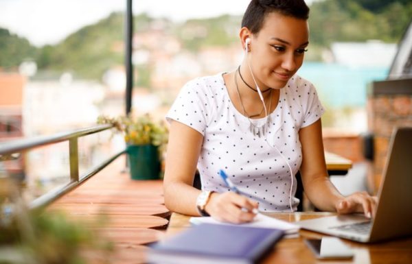 une femme qui prend des notes tout en utilisant son ordinateur portable