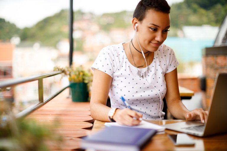 une femme qui prend des notes tout en utilisant son ordinateur portable